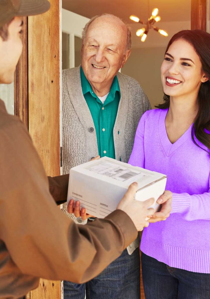 A young woman happily receiving a package at the door from a delivery person.